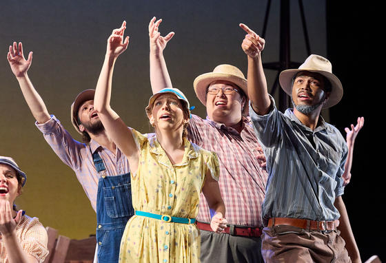 Theater students in a group dressed in period dress costume with arms raised in the air
